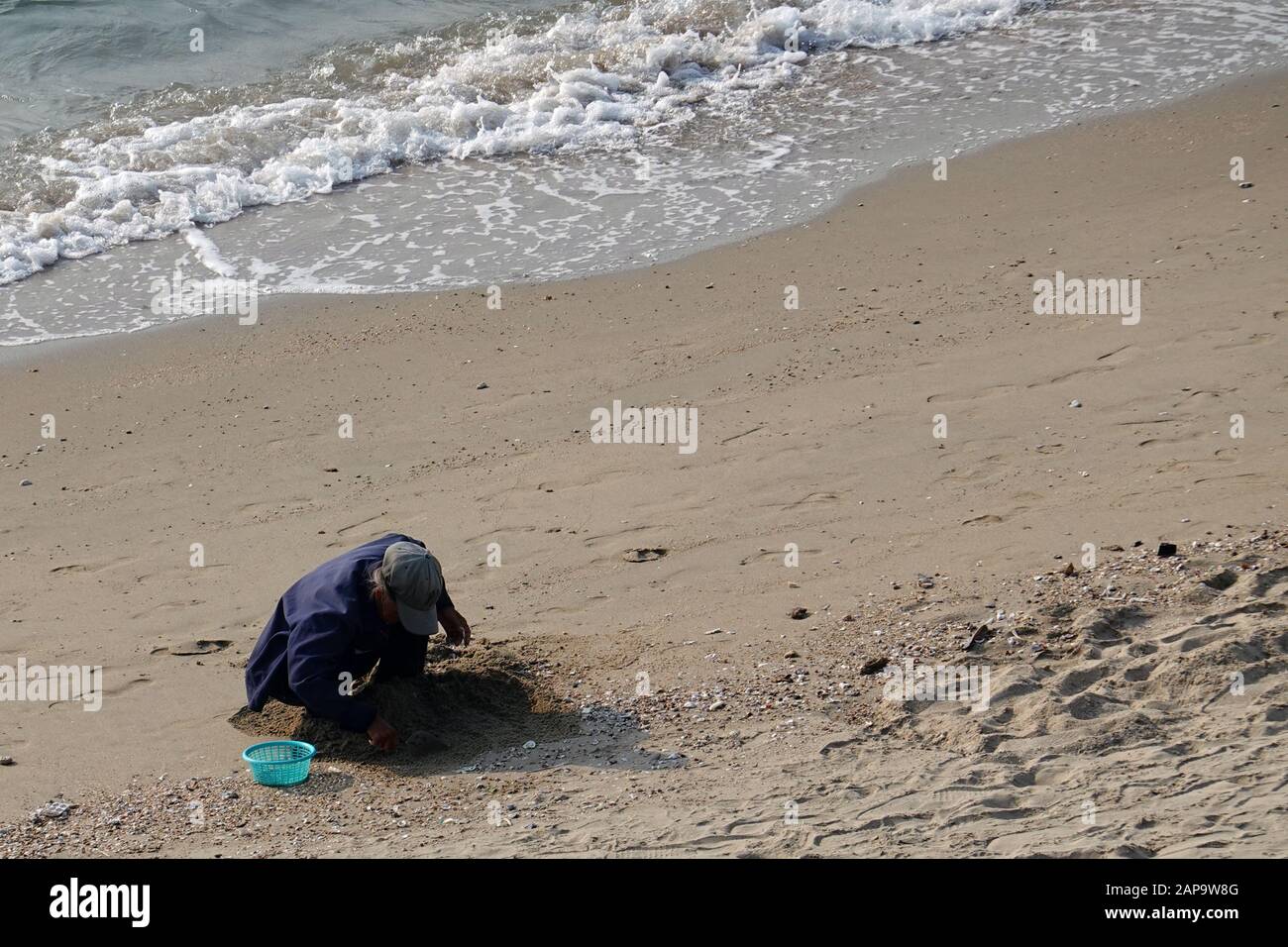 Pattaya, Thailandia - 23 dicembre 2019: Donna anziana seduta sulla spiaggia e cercando di trovare vongole. Foto Stock