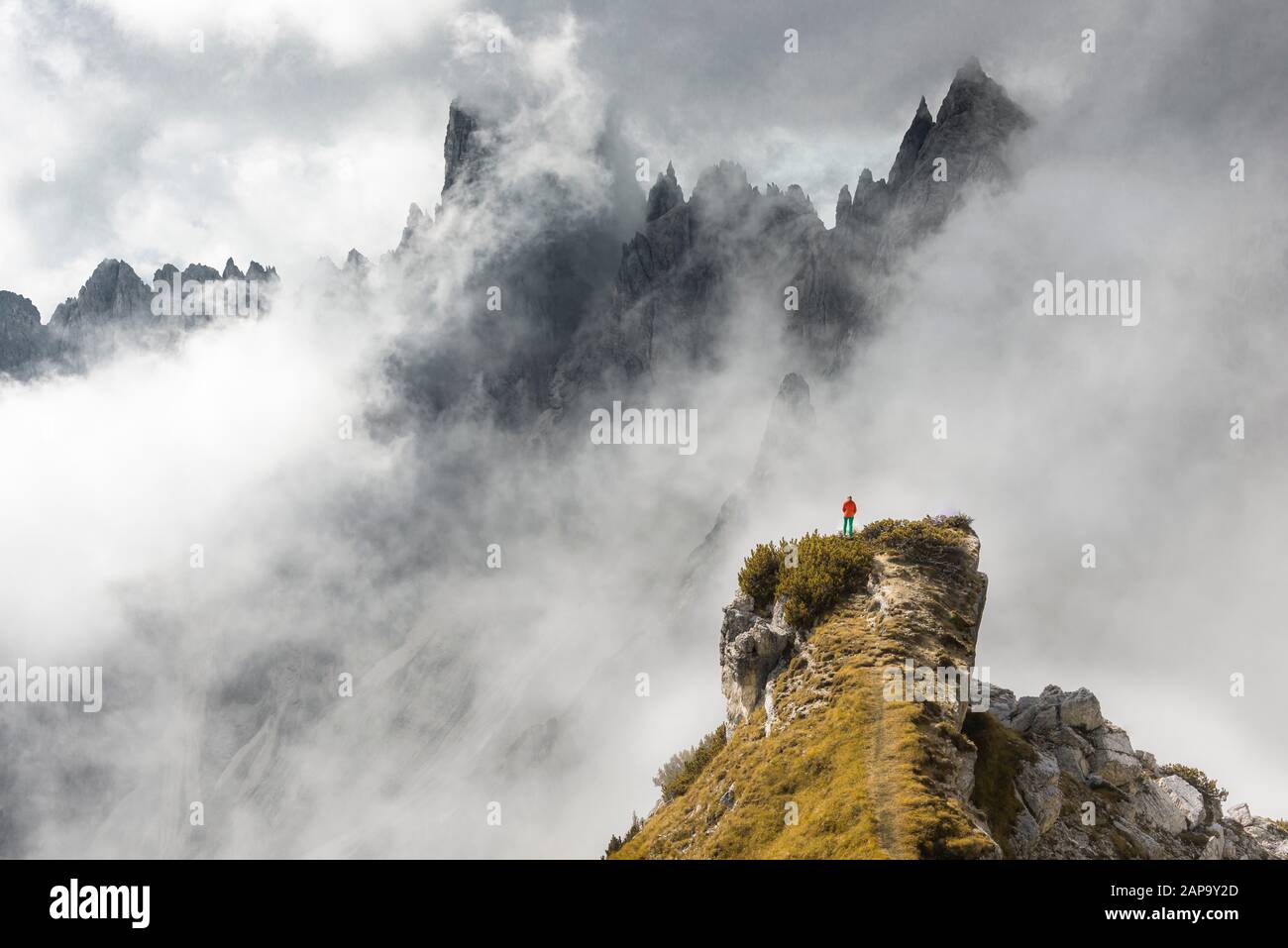 L'alpinista si erge su un crinale, dietro le cime montuose e le rocce appuntite, le nuvole drammatiche, il Cimon di Croda liscia e il Gruppo Cadini, Auronzo di Cadore Foto Stock
