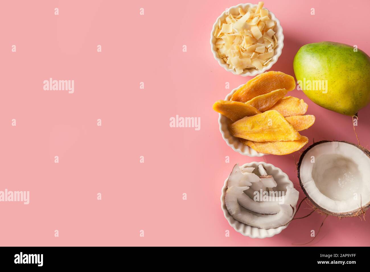 Disidratato ed essiccato di mango e scaglie di noce di cocco nella ciotola bianco su sfondo rosa. Vista da sopra. Foto Stock