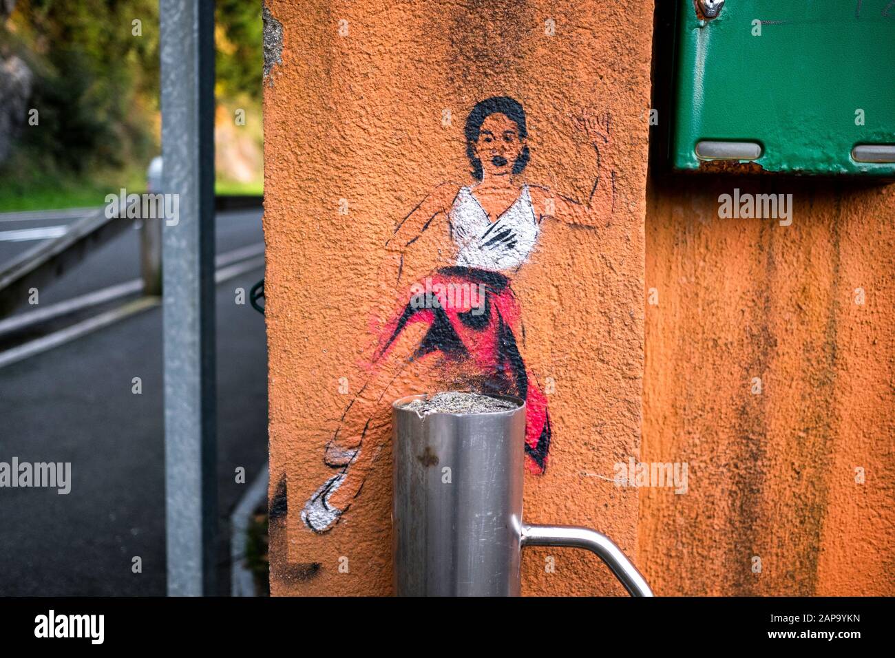 Pin-up ragazza swing ballerina femminile che disegna graffiti in un muro accanto a una strada in Urdaibai. Street art. Foto Stock