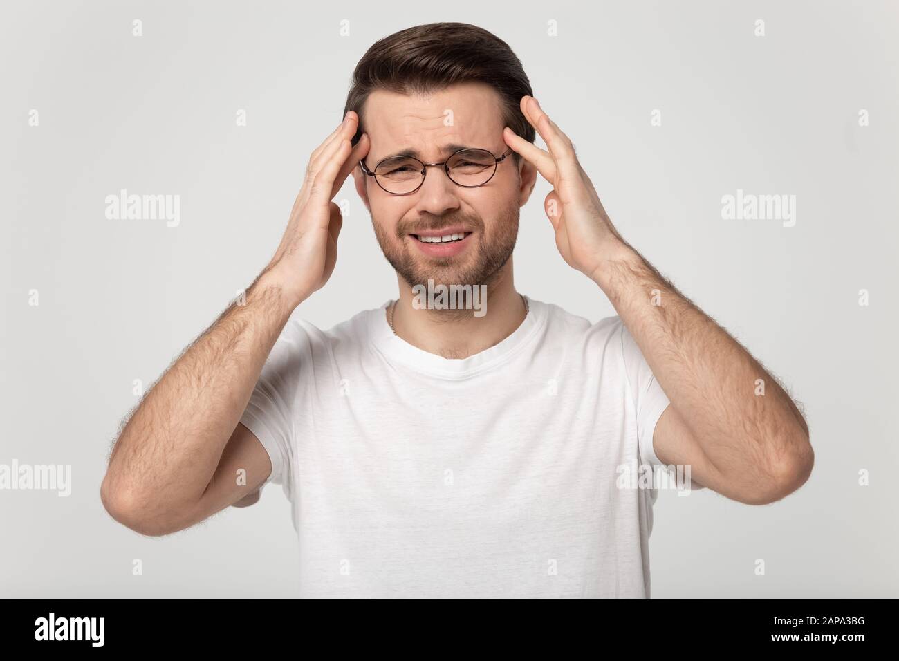 Uomo millenario stanco che massaggia i templi, soffrendo di mal di testa improvviso. Foto Stock