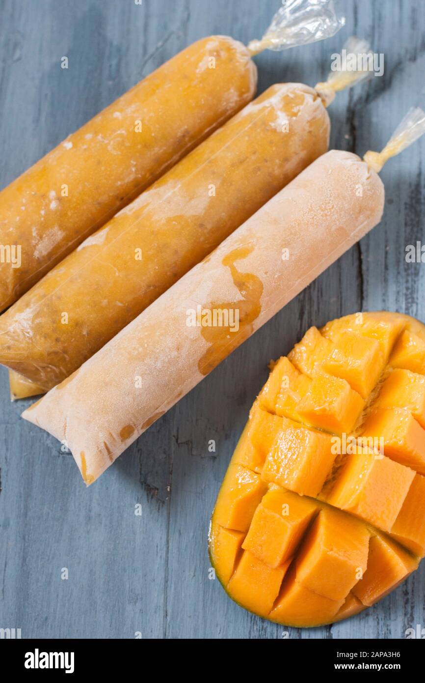 Tre mango chia lolllies su sfondo blu con un mango tagliato a metà Foto Stock