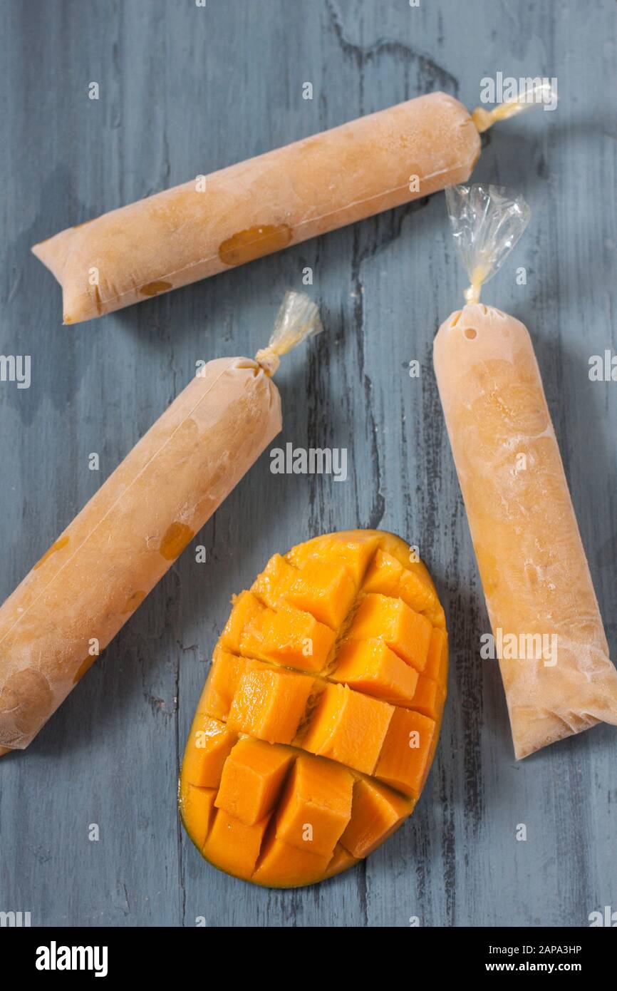 Tre mango chia lolllies su sfondo blu con un mango tagliato a metà Foto Stock