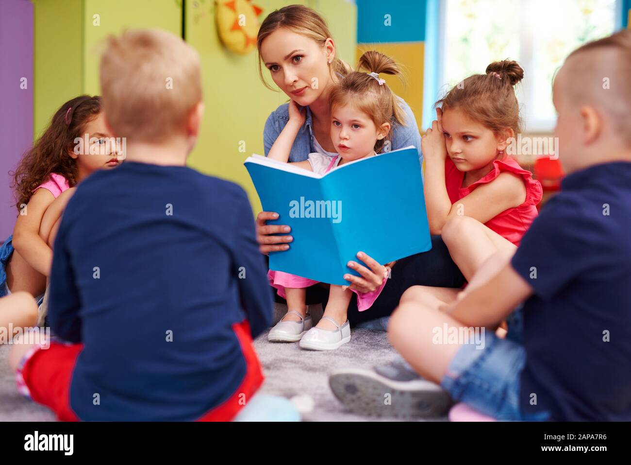 L'insegnante di sesso femminile sta leggendo un libro durante le lezioni in prescolare Foto Stock