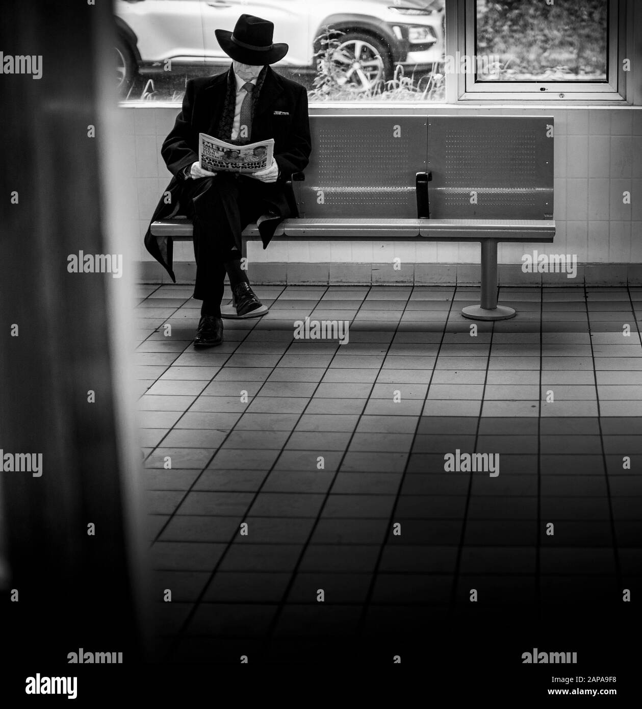Un Signore elegante che indossa un vestito e un cappello legge un giornale si siede in sala d'attesa mentre attende un treno, Kent, Inghilterra UK Foto Stock