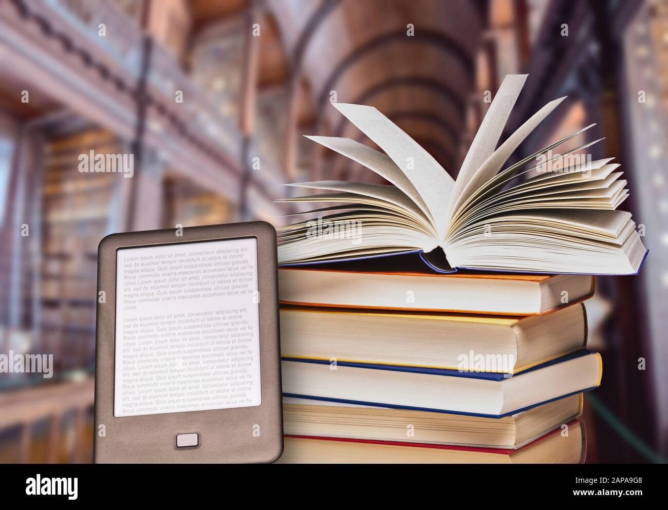 Pila di libri con un libro aperto e lettore di e-book in una grande biblioteca Foto Stock