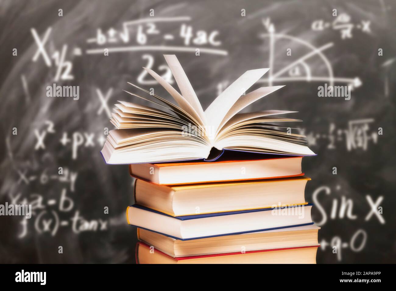 Libro aperto su una pila di fronte a una lavagna con formule matematiche Foto Stock