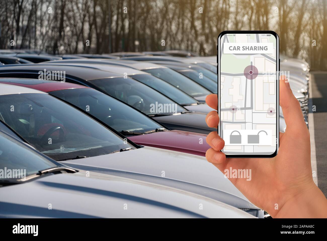 Mano con telefono su uno sfondo di auto parcheggiate. Applicazione mobile per la condivisione delle auto. Condivisione Del Carico. Foto Stock