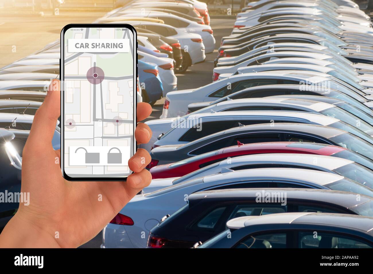 Mano con telefono su uno sfondo di auto parcheggiate. Applicazione mobile per la condivisione delle auto. Condivisione Del Carico. Foto Stock
