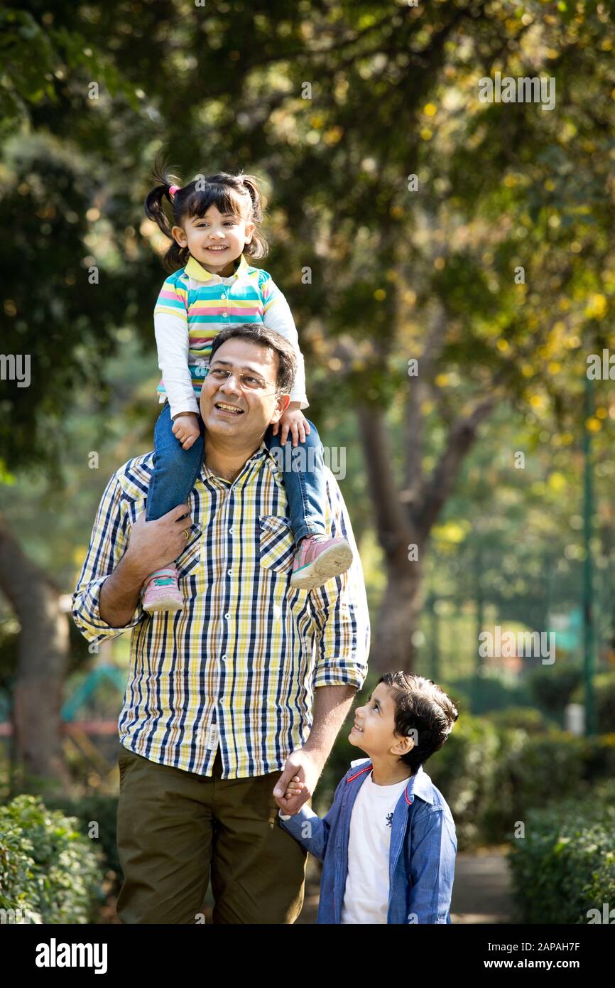 Padre che porta la figlia sulle spalle e tiene le mani del figlio al parco Foto Stock