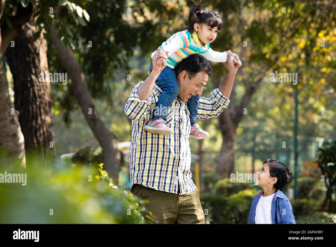 Padre che porta la figlia sulle spalle e tiene le mani del figlio al parco Foto Stock