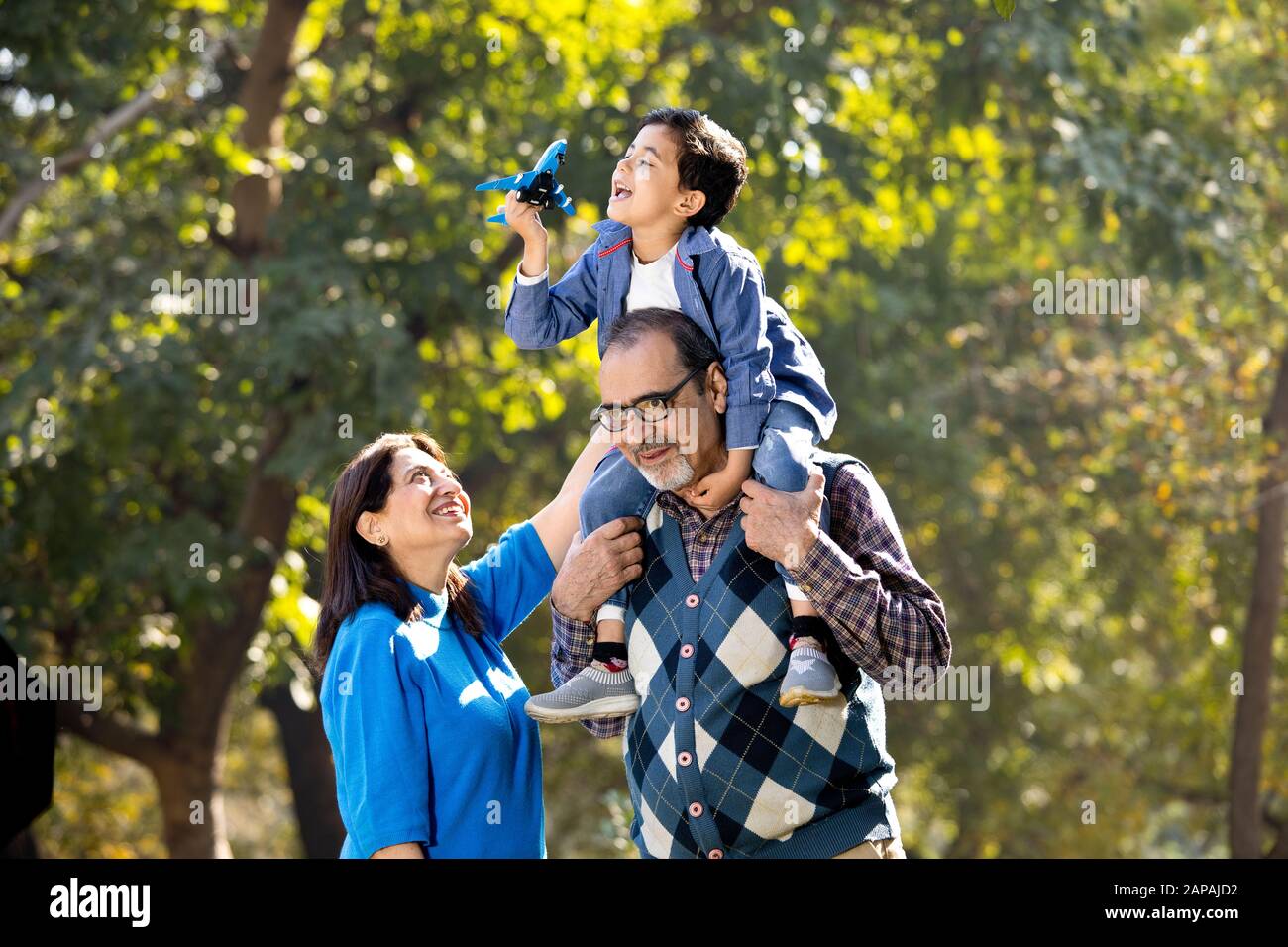 Nonna con ragazzo che tiene l'aeroplano giocattolo seduto sulla spalla del nonno al parco Foto Stock