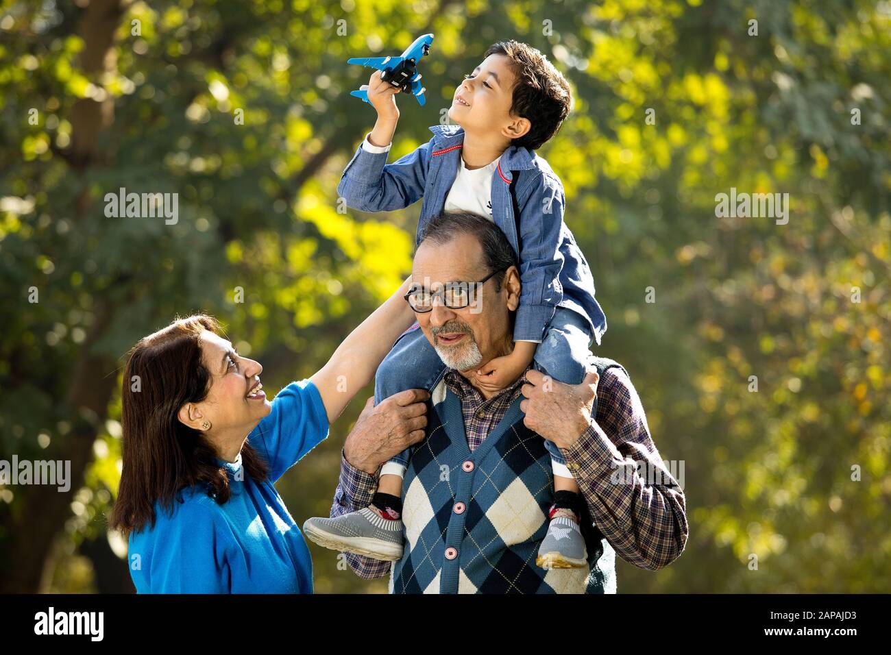 Nonna con ragazzo che tiene l'aeroplano giocattolo seduto sulla spalla del nonno al parco Foto Stock