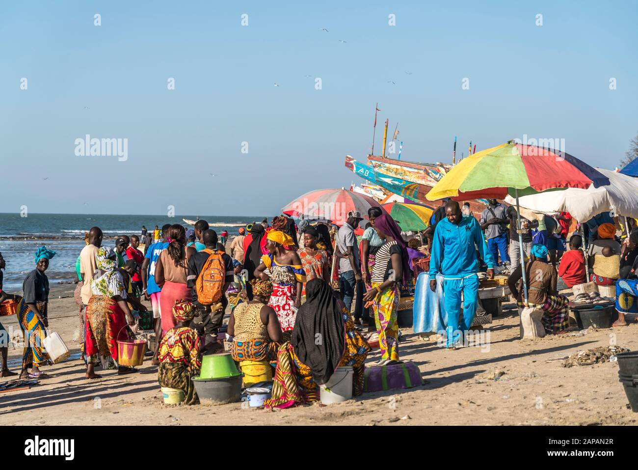 Bunte Kleider und Boote auf dem Fischmarkt a Tanji, Gambia, Westafrika | vestiti colorati e barche al mercato del pesce, Tanji, Gambia, Africa occidentale Foto Stock