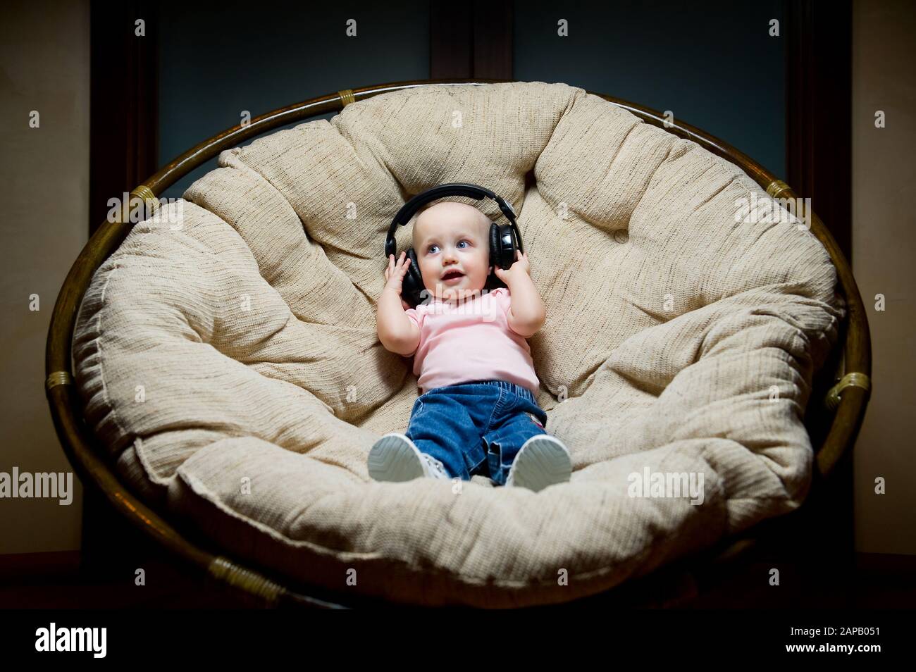 il bambino ascolta la musica in grandi cuffie mentre si siede in una grande poltrona Foto Stock
