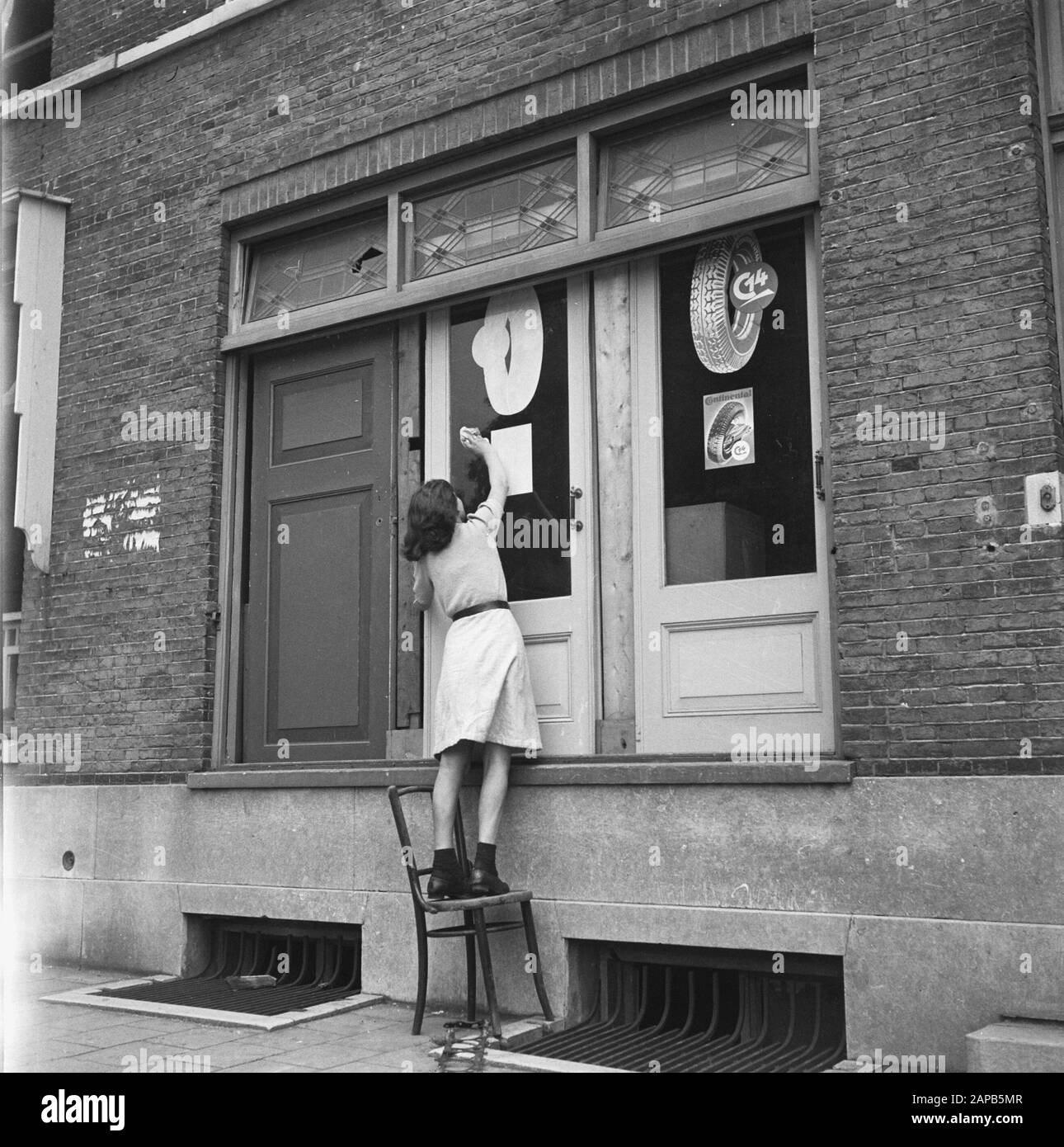 Recupero: Arnhem Descrizione: Le porte (da un garage?) servono come sostituzione dei vetri della finestra. Il vetro di una porta è lucidato da una donna Data: 1945 luogo: Arnhem, Gelderland Parole Chiave: Recupero, seconda guerra mondiale, ricostruzione Foto Stock