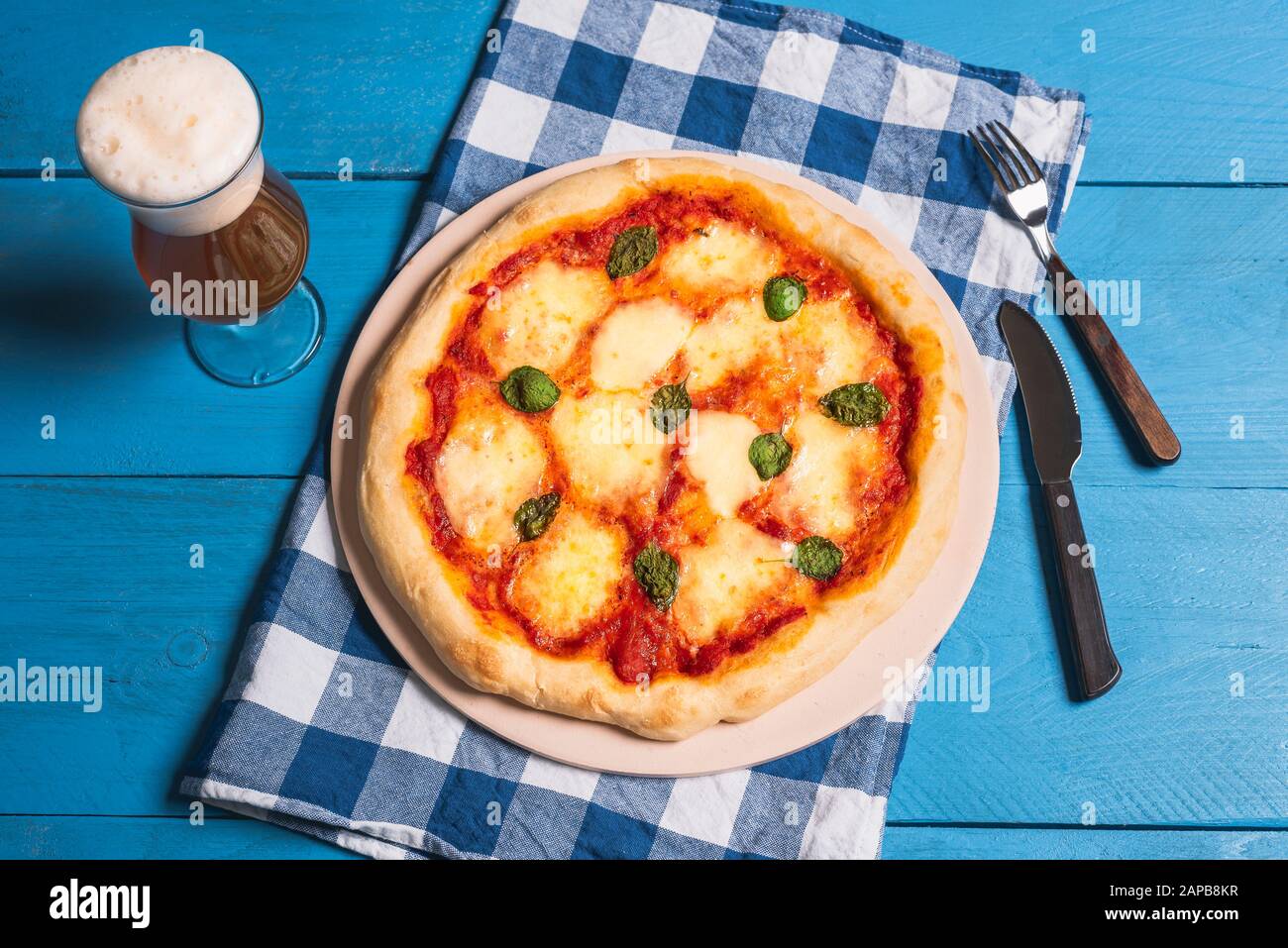 Pizza fresca margarita e birra sul tavolo blu bavarese decorato. Oktoberfest cibo, pizza, birra e tovagliolo blu. Cena tedesca. Pizza al formaggio fuso. Foto Stock