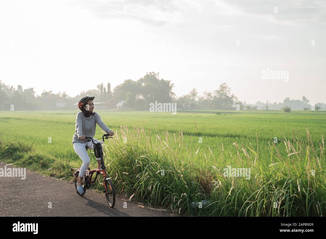 Le donne asiatiche indossano i caschi per guidare le bici pieghevoli nei campi di riso Foto Stock