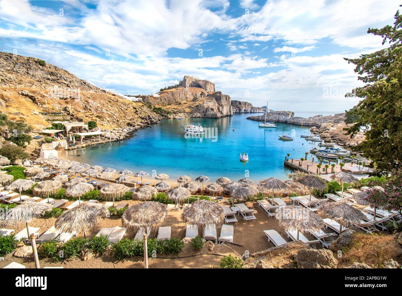 Lindos – vista sulla baia di San Paolo, spiaggia con lettini e ombrelloni, acropoli di Lindos sullo sfondo (Rodi, Grecia) Foto Stock