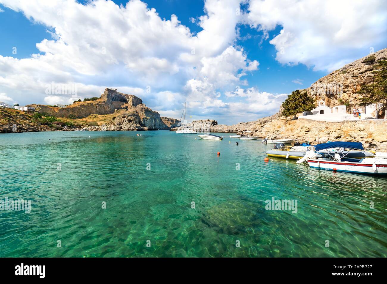Lindos – Vista della baia di San Paolo, barche a motore ancorate vicino alla chiesa ortodossa e acropoli di Lindos sullo sfondo (Rodi, Grecia) Foto Stock