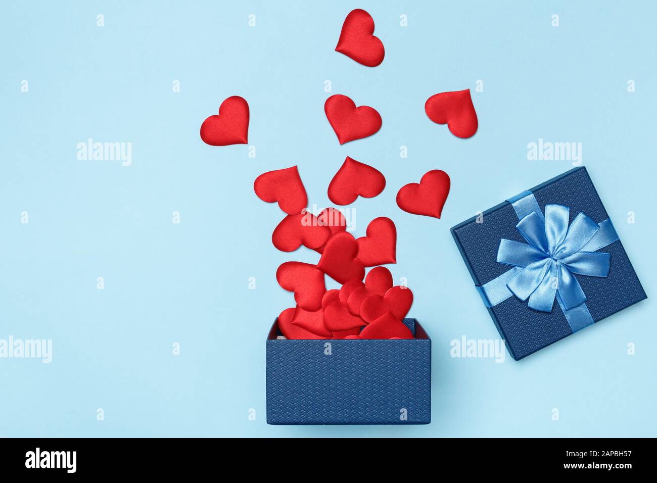 Cuori rossi sparsi da una scatola regalo aperta blu su uno sfondo colorato. Il concetto di amore e San Valentino. Foto Stock