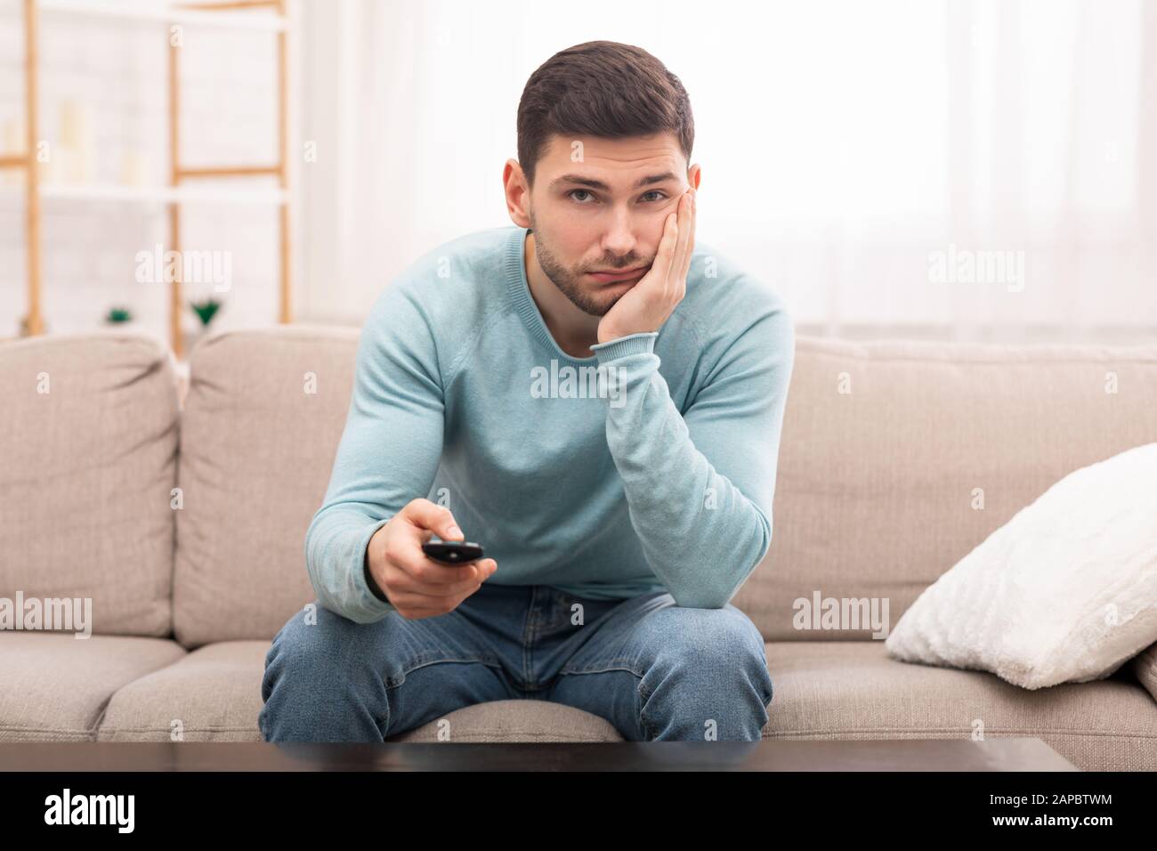 Guy Annoiato Cambio Canali Guardare La Tv Seduto Sul Divano Interno Foto Stock