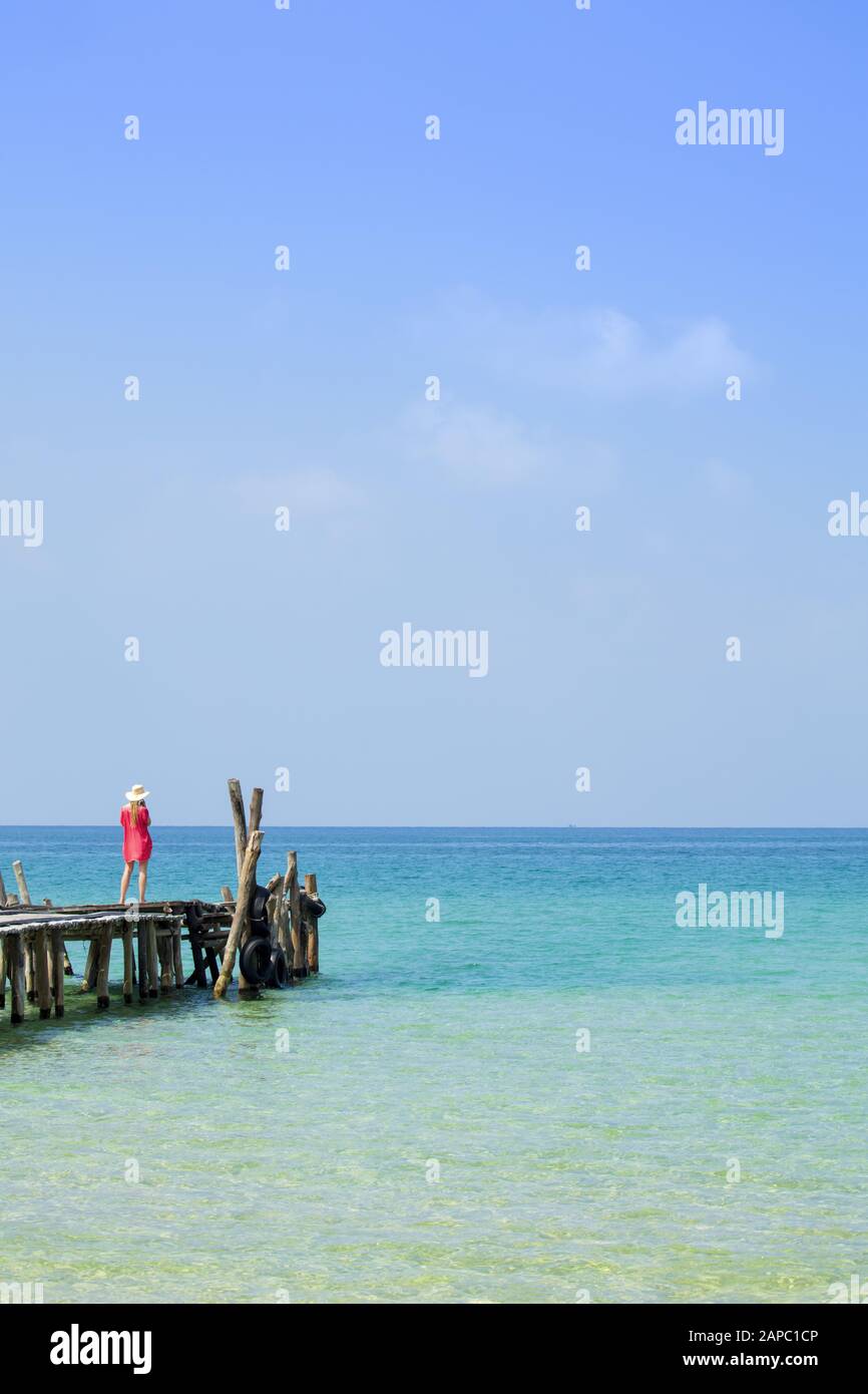 Isole Rong. Una giovane donna in costume da bagno rosso e cappello da spiaggia in piedi su un molo di barca sopra l'Oceano Indiano turchese Foto Stock