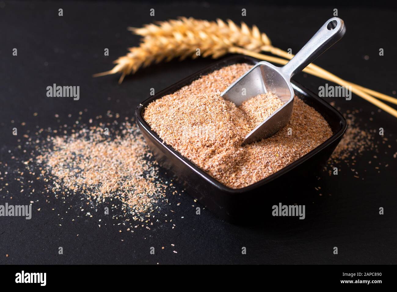 Concetto di cibo sano Crusca Di Grano Organico in tazza di ceramica nera con l'orecchio di grano su fondo di pietra di ardesia nera Foto Stock