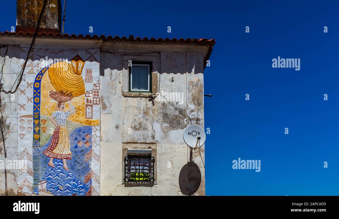 Bianco, casa dilapidata nel quartiere di Alfama con murale colorato sulla sua parete su sfondo cielo blu chiaro. Foto Stock