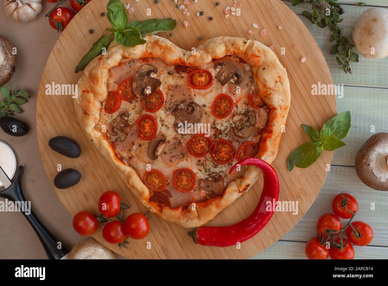 La Pizza a forma di cuore con prosciutto pomodori e funghi su sfondo di legno . Concetto di amore romantico per il giorno di San Valentino . Amore cibo Foto Stock