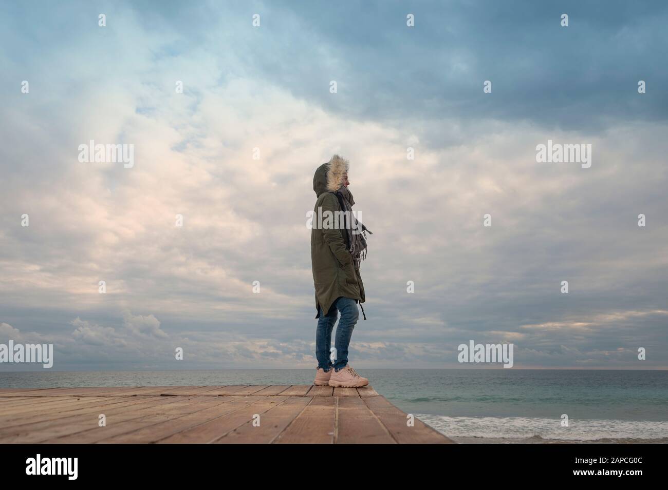 donna che indossa un cappotto parka che si affaccia sul mare, da sola. Foto Stock