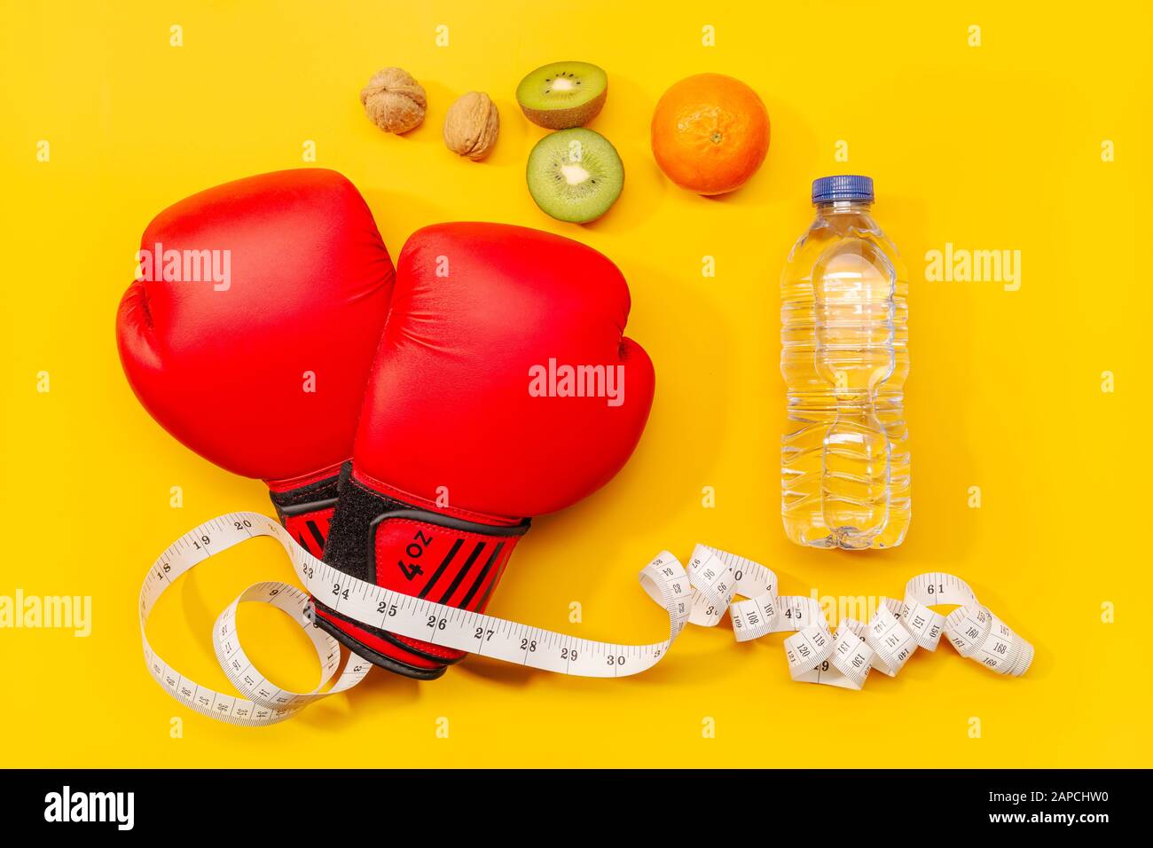 Fitness, perdita di peso o concetto di esercizio. Guanti da boxe, alimenti sani e metro a nastro isolato su sfondo giallo Foto Stock