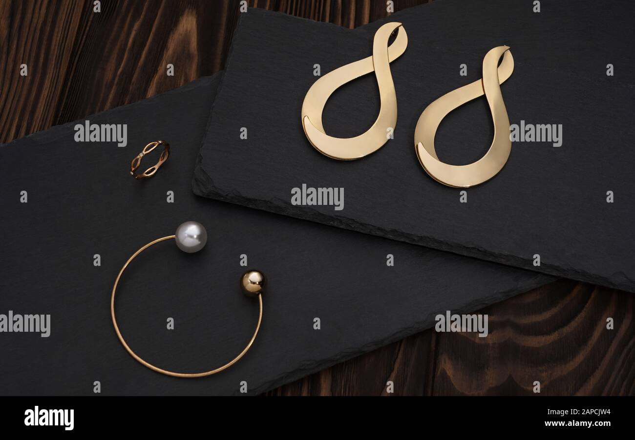 Bracciale dorato, anello ed orecchini si accoppiano su piatto nero Foto Stock