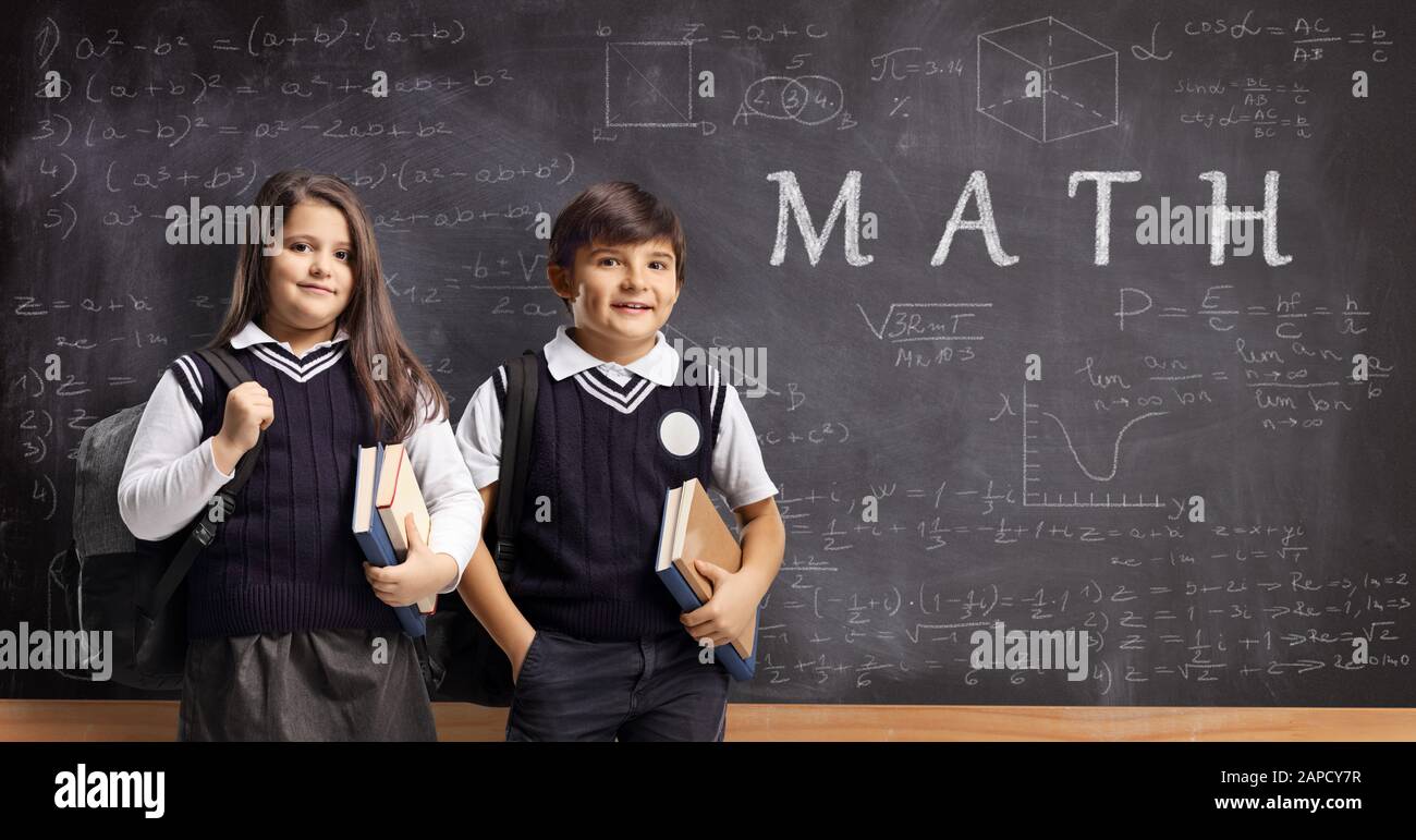 Scolari e scolaresche in uniformi che si trovano di fronte a una lavagna con formule matematiche e testi scritti di matematica Foto Stock