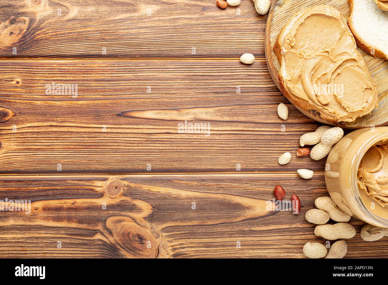 Toast con burro di arachidi. Cucchiaio e vasetto di burro di arachidi e arachidi per la prima colazione su fondo di legno marrone. Pasta di arachidi cremosa Foto Stock