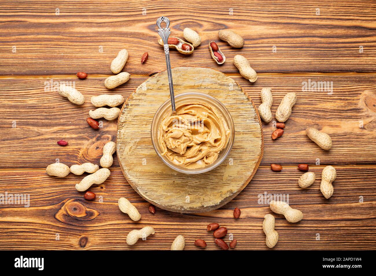 Toast con burro di arachidi. Cucchiaio e vasetto di burro di arachidi e arachidi per la prima colazione su fondo di legno marrone. Pasta di arachidi cremosa Foto Stock