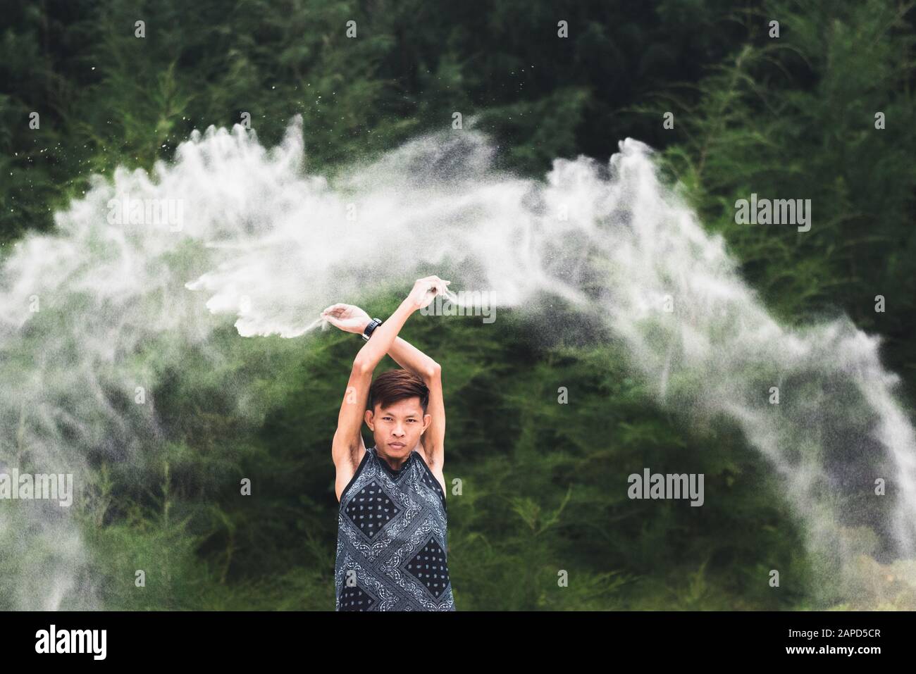Splash di creatività e gioia. Il giovane asiatico getta sabbia bianca fine in aria con le sue mani in testa. Espressione di sé di un millenario Foto Stock
