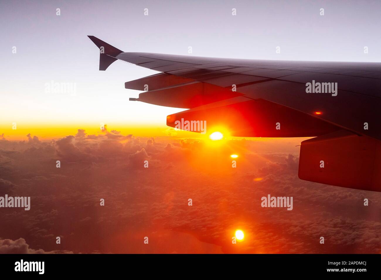 Il sole si cala da sotto l'ala di un aereo su un volo internazionale a lungo raggio. Un cludscape di soffici nuvole di cumuli è molto al di sotto. Foto Stock