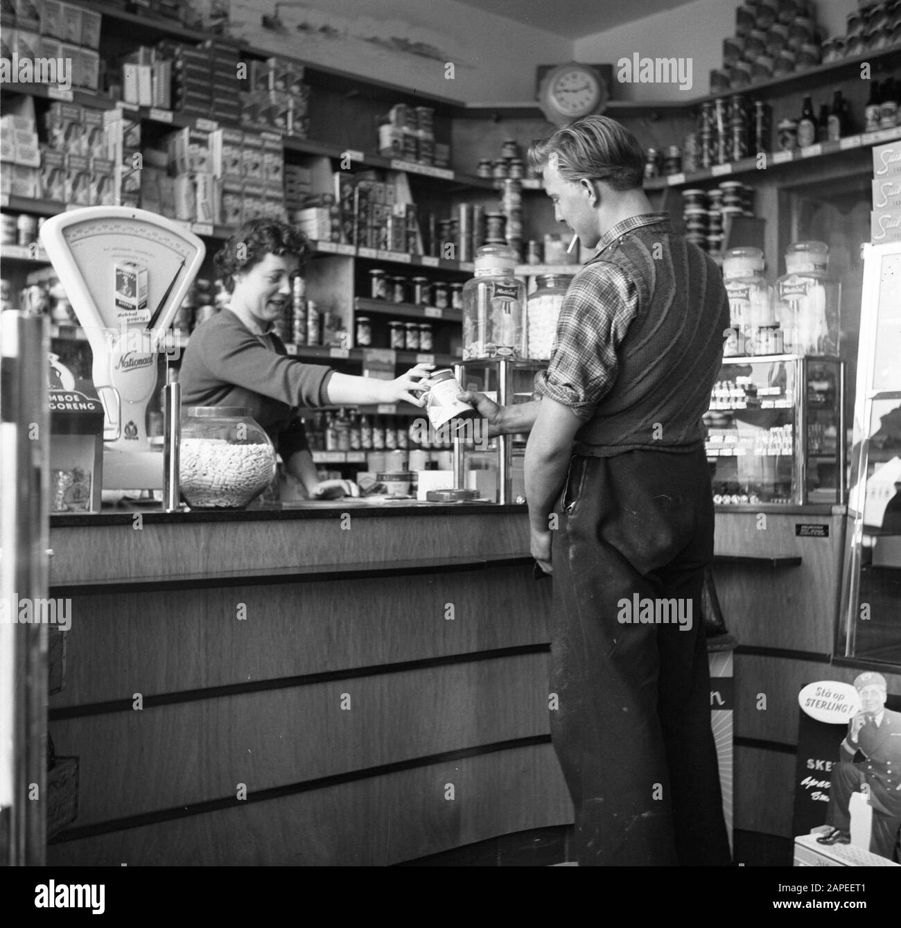 Rijnvaart, report on living and working on board a Rhine ship Descrizione: Membro dell'equipaggio Arthur fa shopping in un negozio di alimentari Data: 1 aprile 1955 posizione: Rotterdam, Zuid-Holland Parole Chiave: Alimentari, vita quotidiana, negozio di alimentari, skipper, negozi Foto Stock