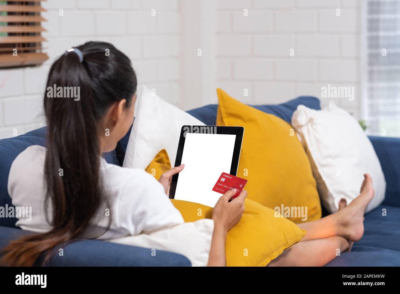 Giovane donna asiatica shopping online con carta di credito e utilizzando tablet con mockup blank sceen.Cosy su sofà.shopping online concetto Foto Stock