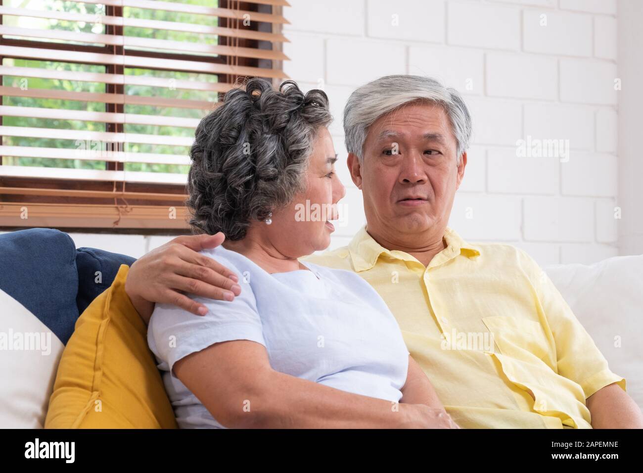 Asian coppia senior abbracciando e sedendo comodamente sul divano e parlando nel soggiorno a casa. Foto Stock