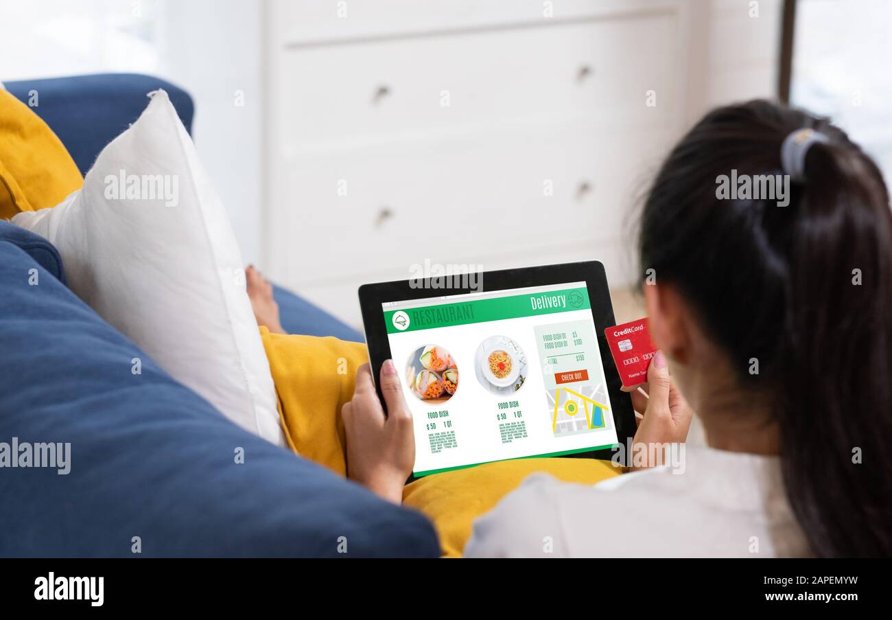 Donna asiatica ordinare cibo online con carta di credito sul tablet seduto sul divano a casa.stile di vita digitale con tecnologia Foto Stock
