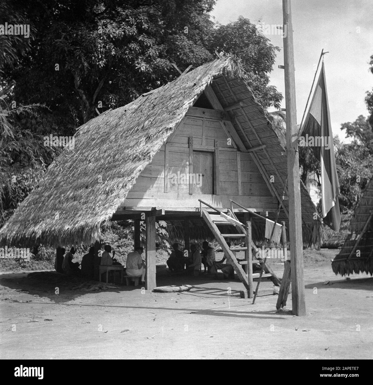 Viaggio nel Suriname e nelle Antille Olandesi Descrizione: Incontro sotto una pole house a Langetabbetje in Suriname. La bandiera olandese si blocca. Date: 1947 Location: Langatabbetje, Marowijne, Suriname Keywords: Raduni, capanne, popolazioni indigene, bandiere Foto Stock
