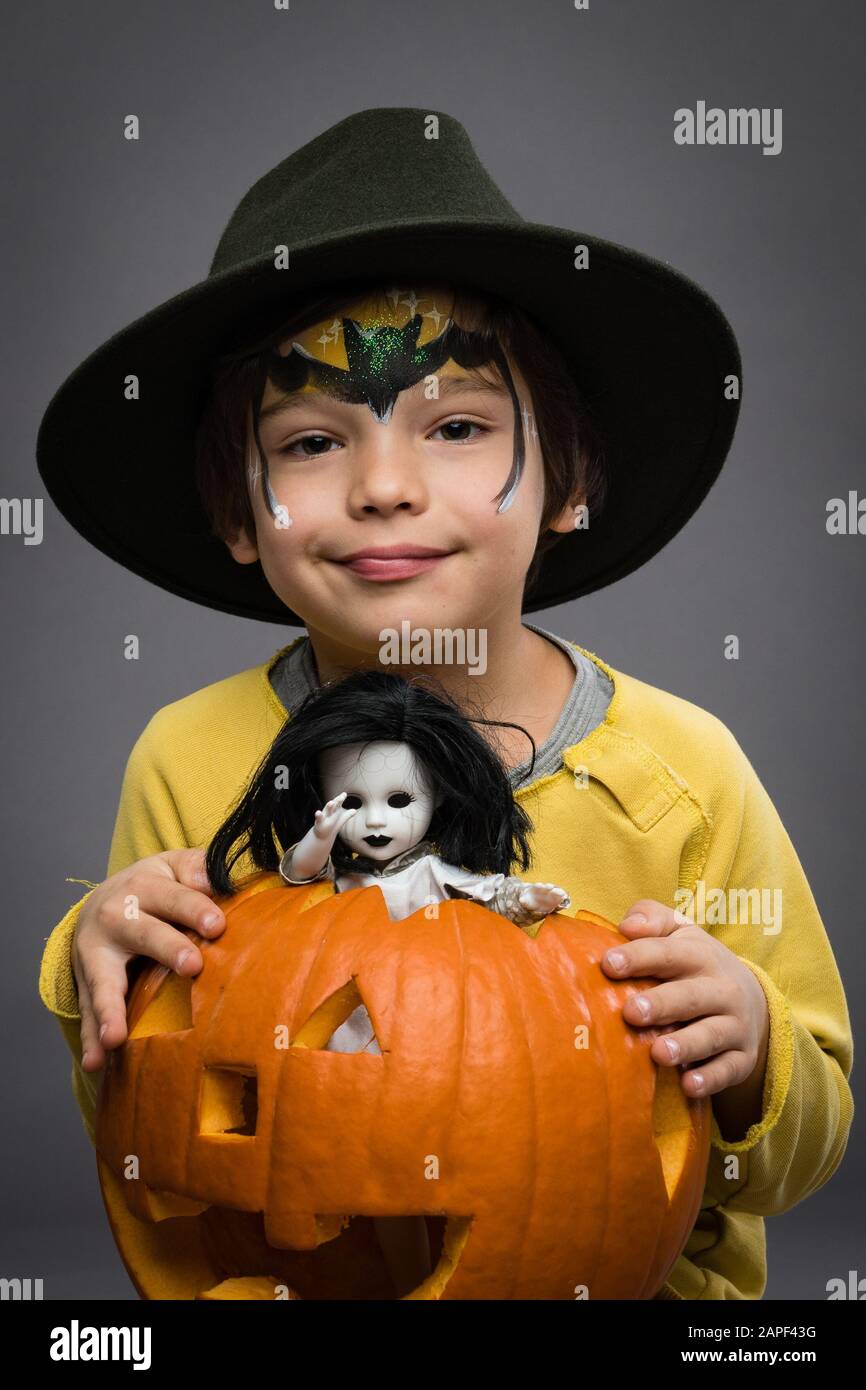 Allegro piccolo boyin un cappello tiene una zucca con la bambola spaventosa su uno sfondo grigio. Halloweencelebration. Foto Stock