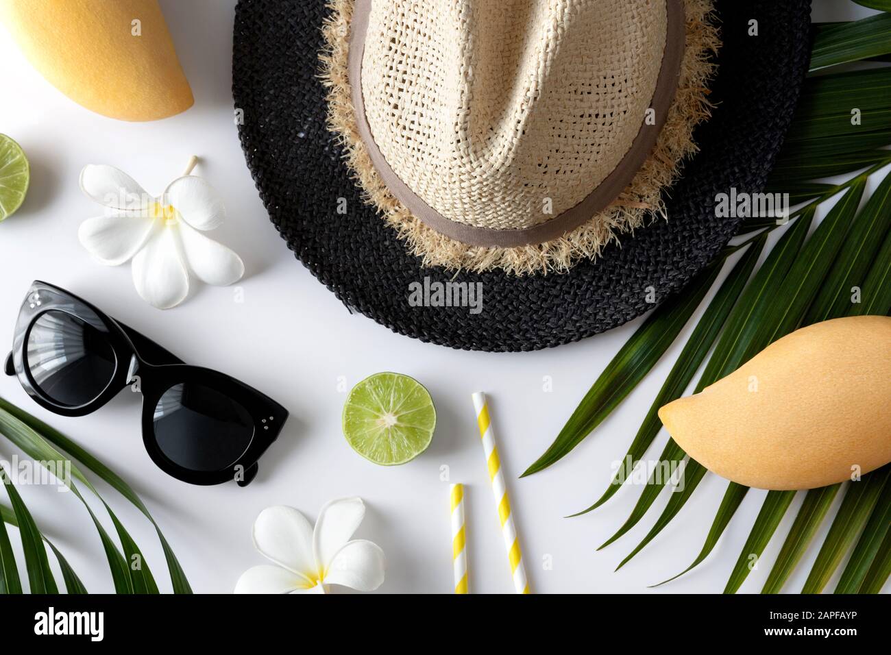 Composizione estiva con frutta, cappello, foglia di palma tropicale e fiori su sfondo bianco Foto Stock