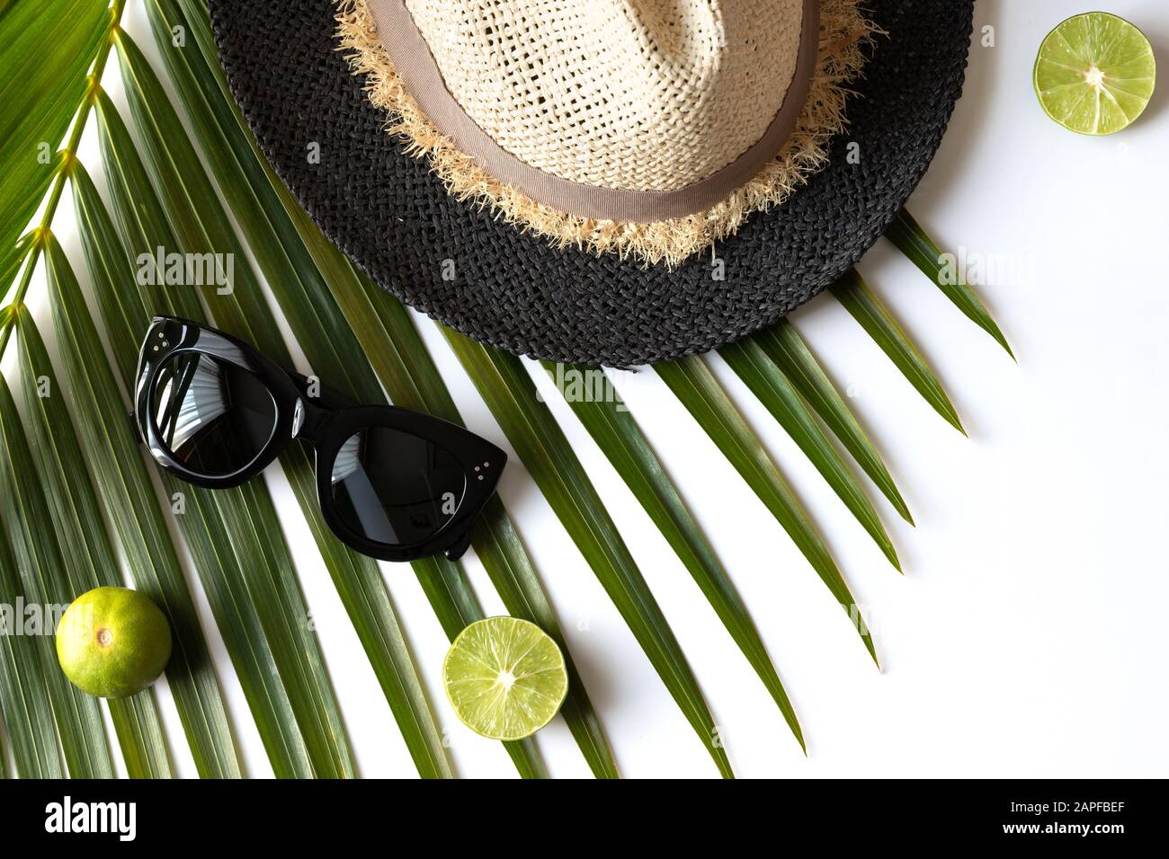 Composizione estiva con frutta, cappello e foglia di palma tropicale su sfondo bianco. Foto Stock