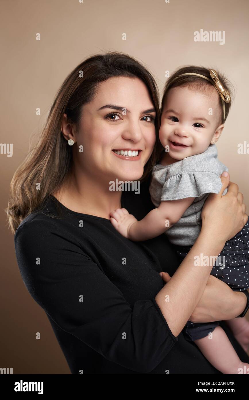 Mamma che tiene piccola bambina su sfondo marrone studio Foto Stock