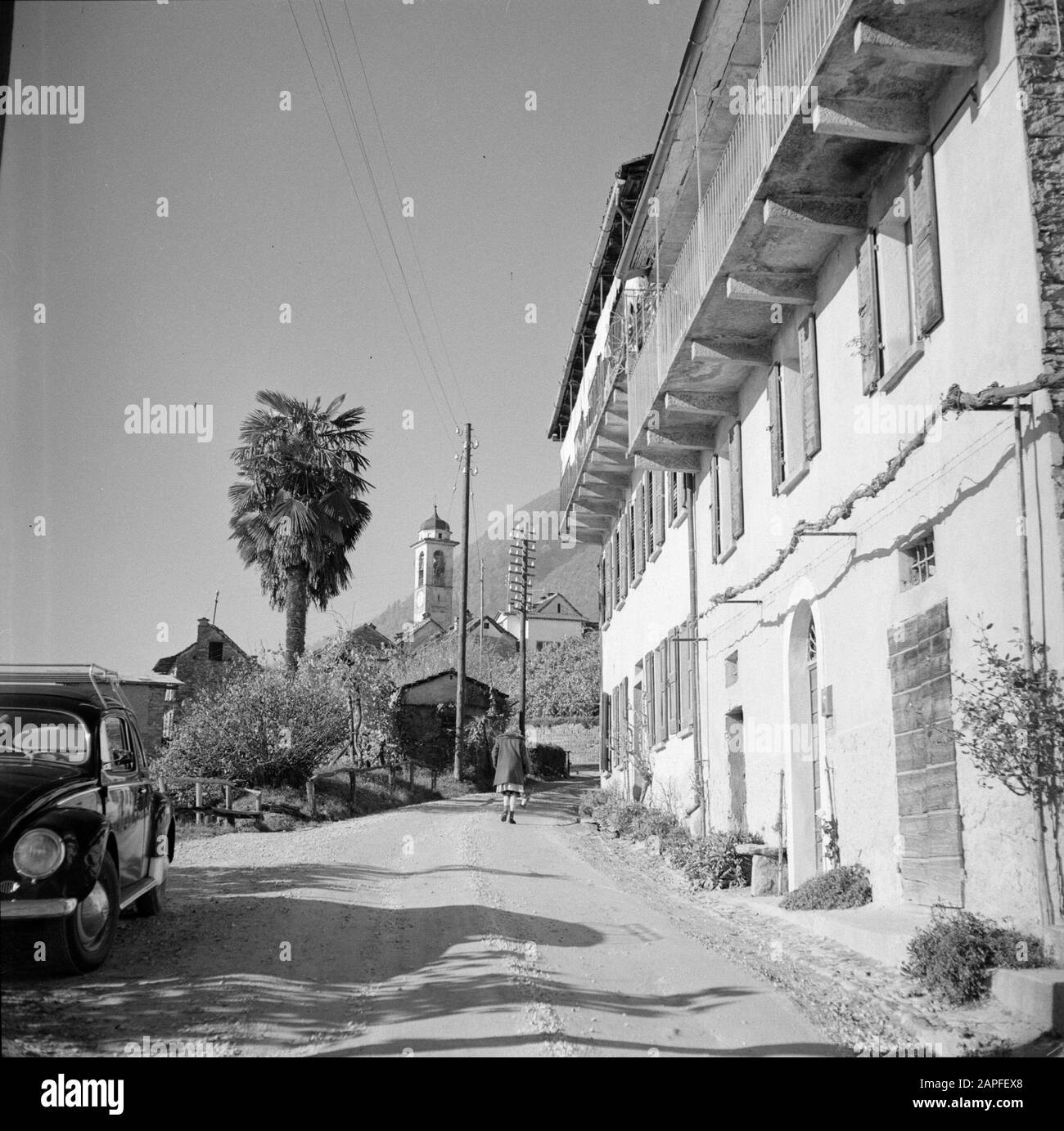 Tour lungo il lato svizzero del Lago maggiore Descrizione: Brione: Strada con case a schiera, piccola chiesa in background Data: Novembre 1961 Località: Brione sopra Minusio, Svizzera Parole Chiave: Automobili, edifici religiosi, statue di strada, case Foto Stock
