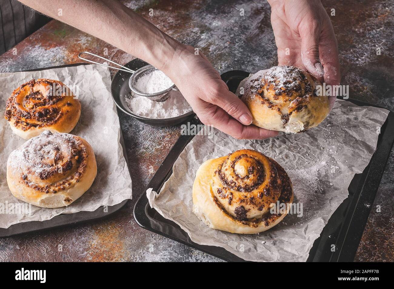 Le mani femminili tengono un rotolo di cannella fresco dolce fatto in casa con crema di cioccolato. Cucina scandinava. Stile Hyugge Foto Stock