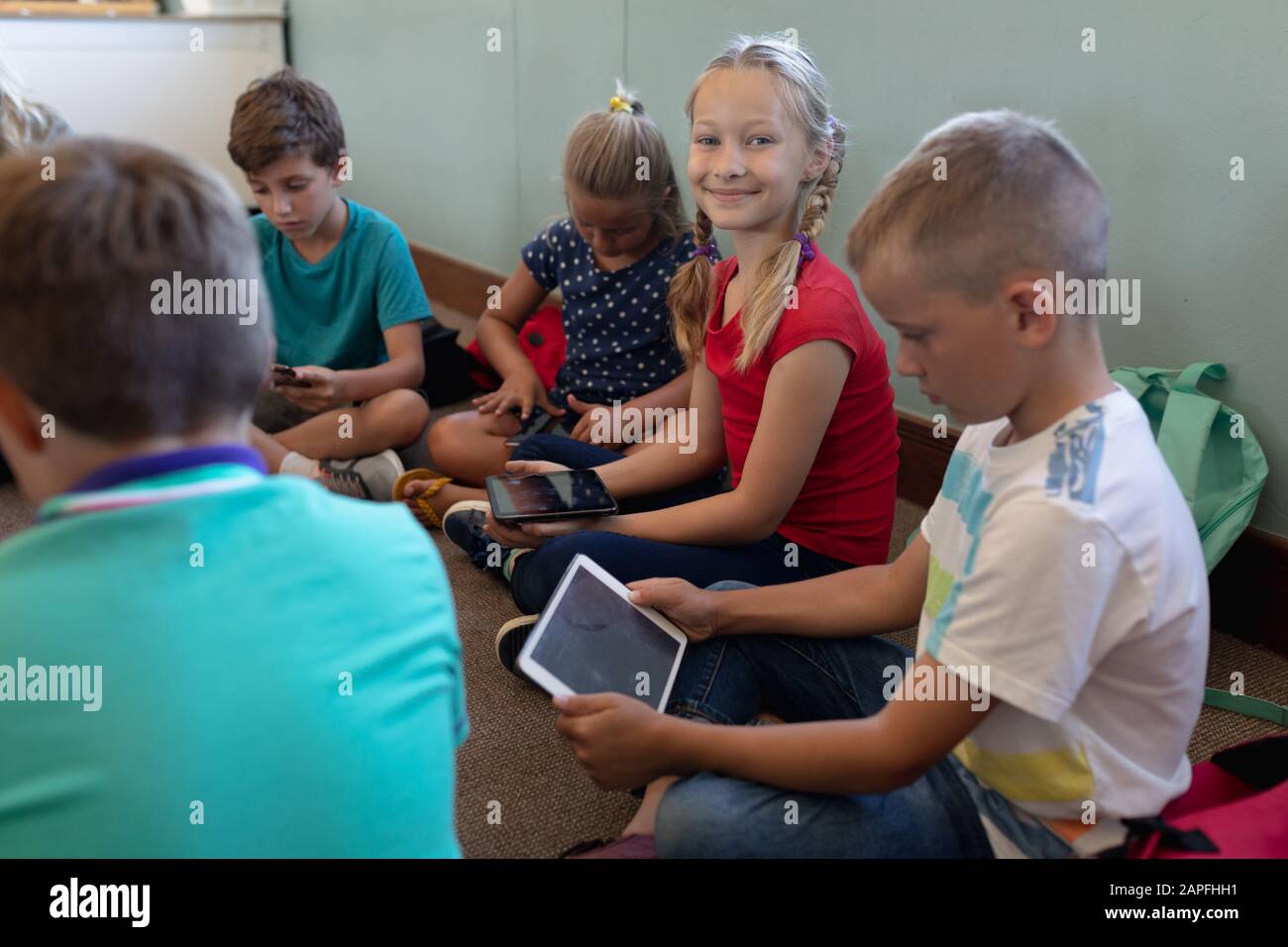 Scolari seduti a gambe incrociate sul pavimento utilizzando un computer tablet in una scuola elementare classro Foto Stock